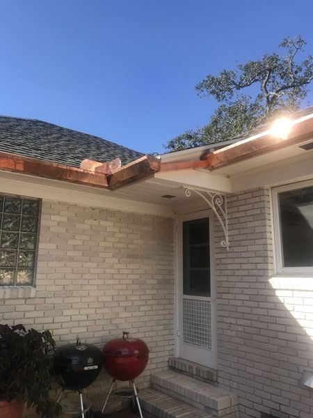 A brick home with a damaged gutter, two grills, and a sunny sky.