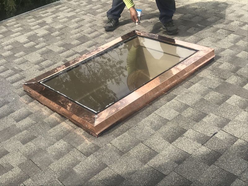 A copper-framed skylight installed on a shingled roof; a worker points toward it.