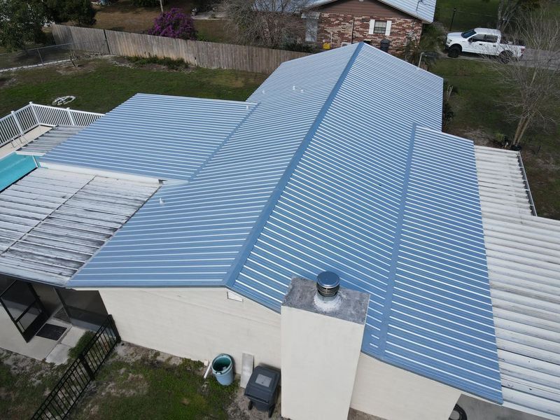 Blue metal roof on a house with a white deck and chimney; a truck is parked nearby.