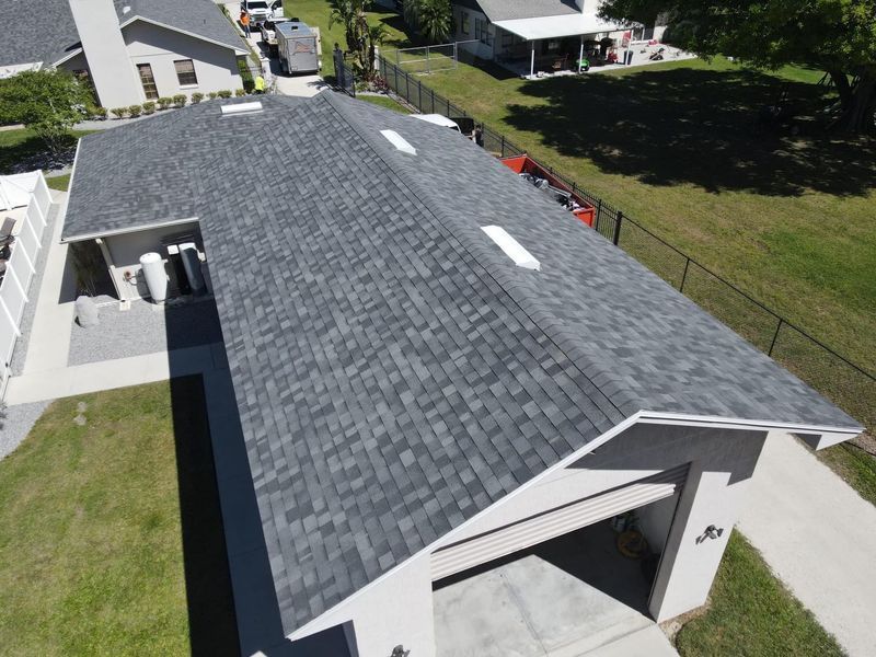 Overhead view of a house with a gray shingle roof, garage, and driveway on a green lawn.