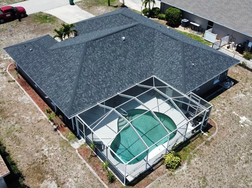 Aerial view of a home with a pool enclosed in a screen. The roof is dark grey, pool is turquoise.