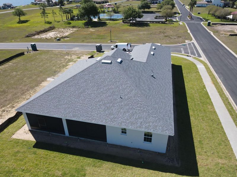 Aerial view of a house with a gray roof on a sunny day, near a street and a lake.