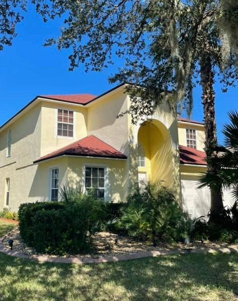 Yellow stucco house with red roof, blue sky, and green shrubbery.