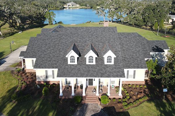 Large yellow house with dark roof, white columns, and a lake in the background.