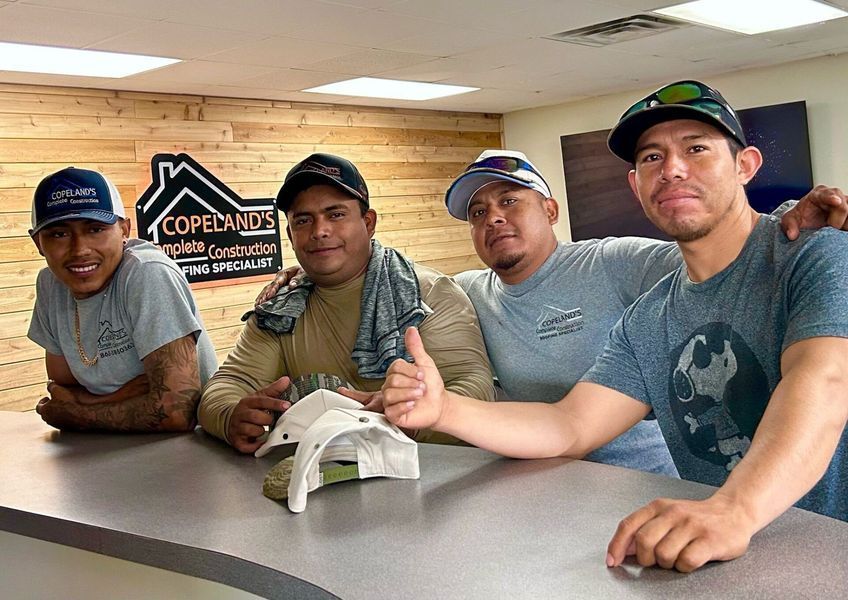 Four construction workers smiling, posing together indoors at a desk.