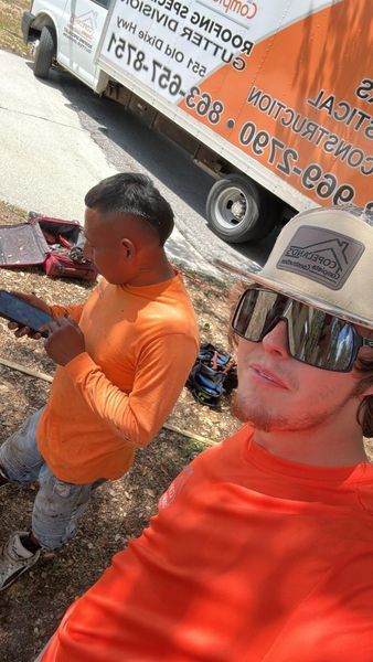 Two construction workers in orange shirts, one holding a tablet, near a white work van with orange text.
