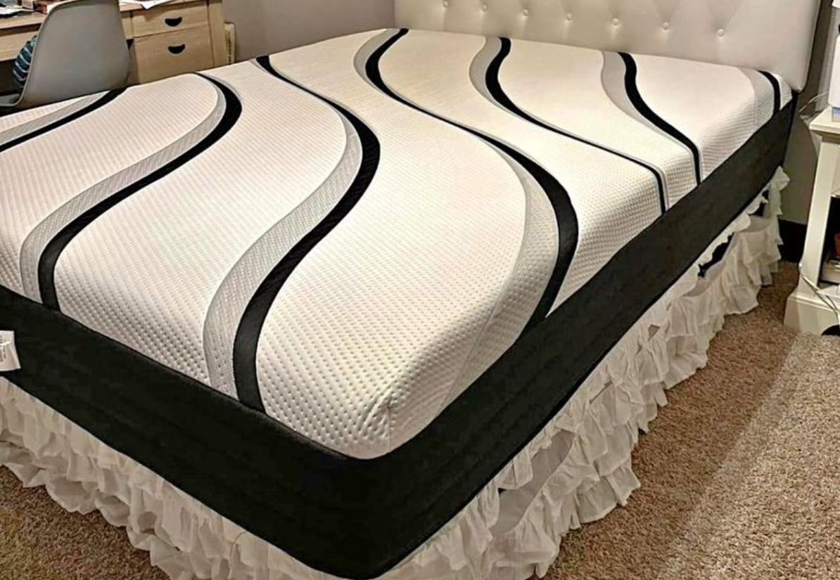 A bed with a white, wavy-patterned mattress and a black border, set in a room with a white headboard and ruffled bed skirt.