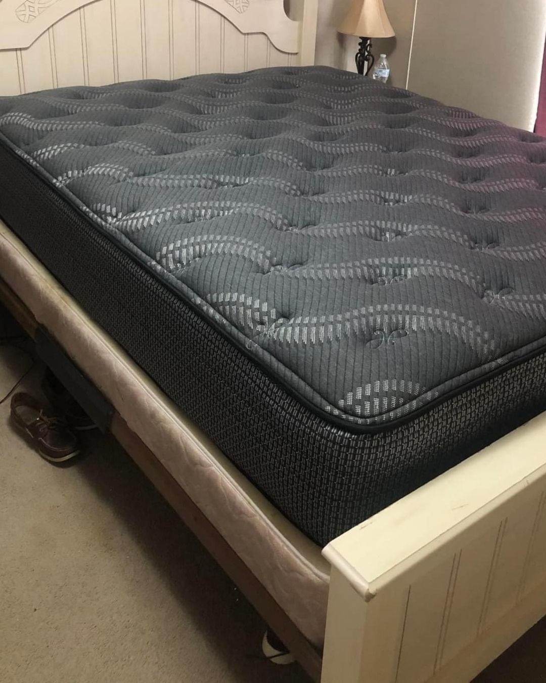 A dark blue mattress stacked on top of a lighter colored mattress on a white bed frame.