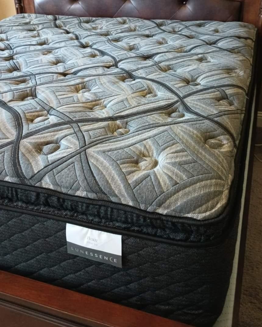 A close-up of a plush, tufted mattress in shades of gray and black on a dark wood bed frame.