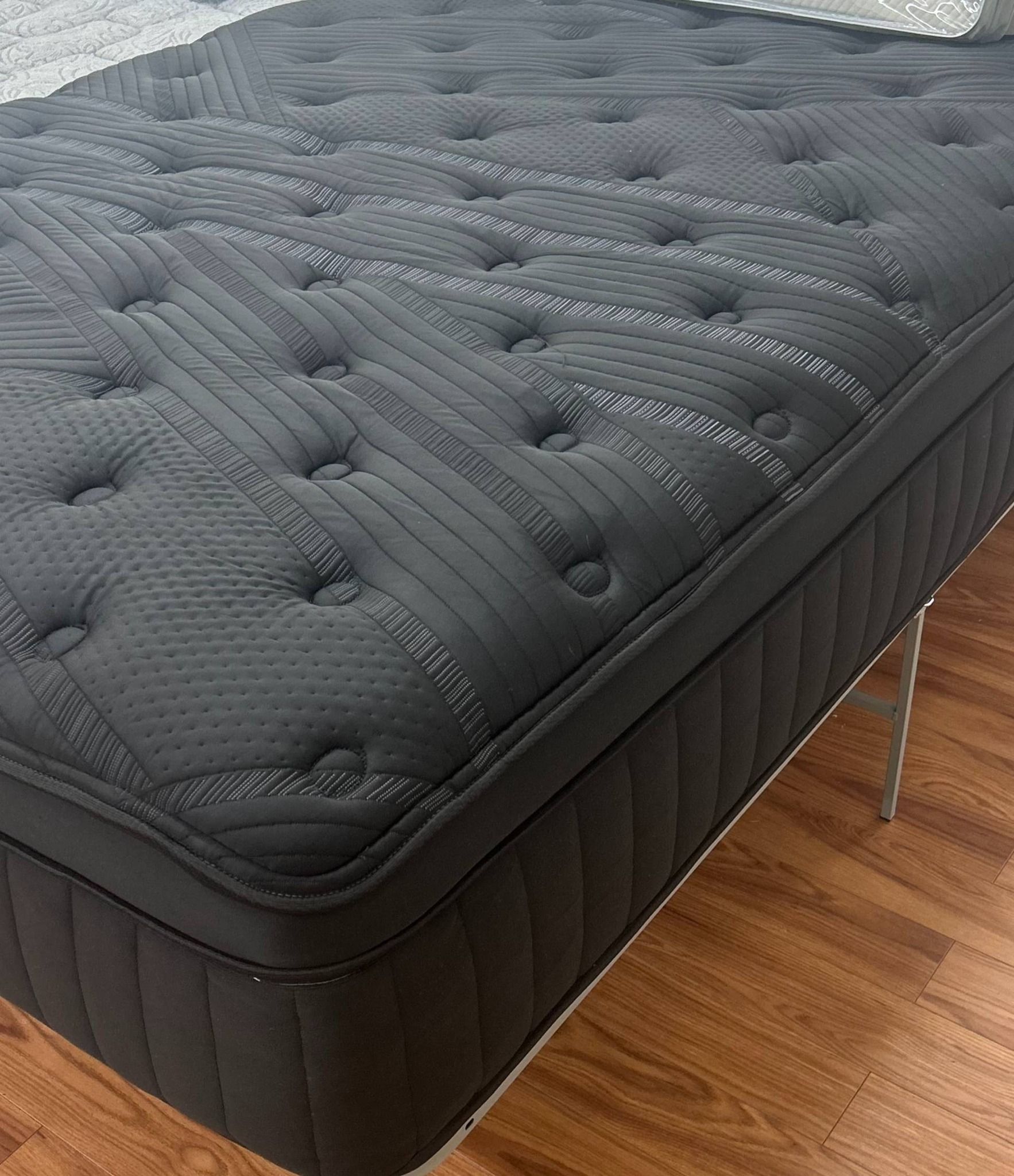 Black tufted mattress on a silver metal base, set against a wood floor.