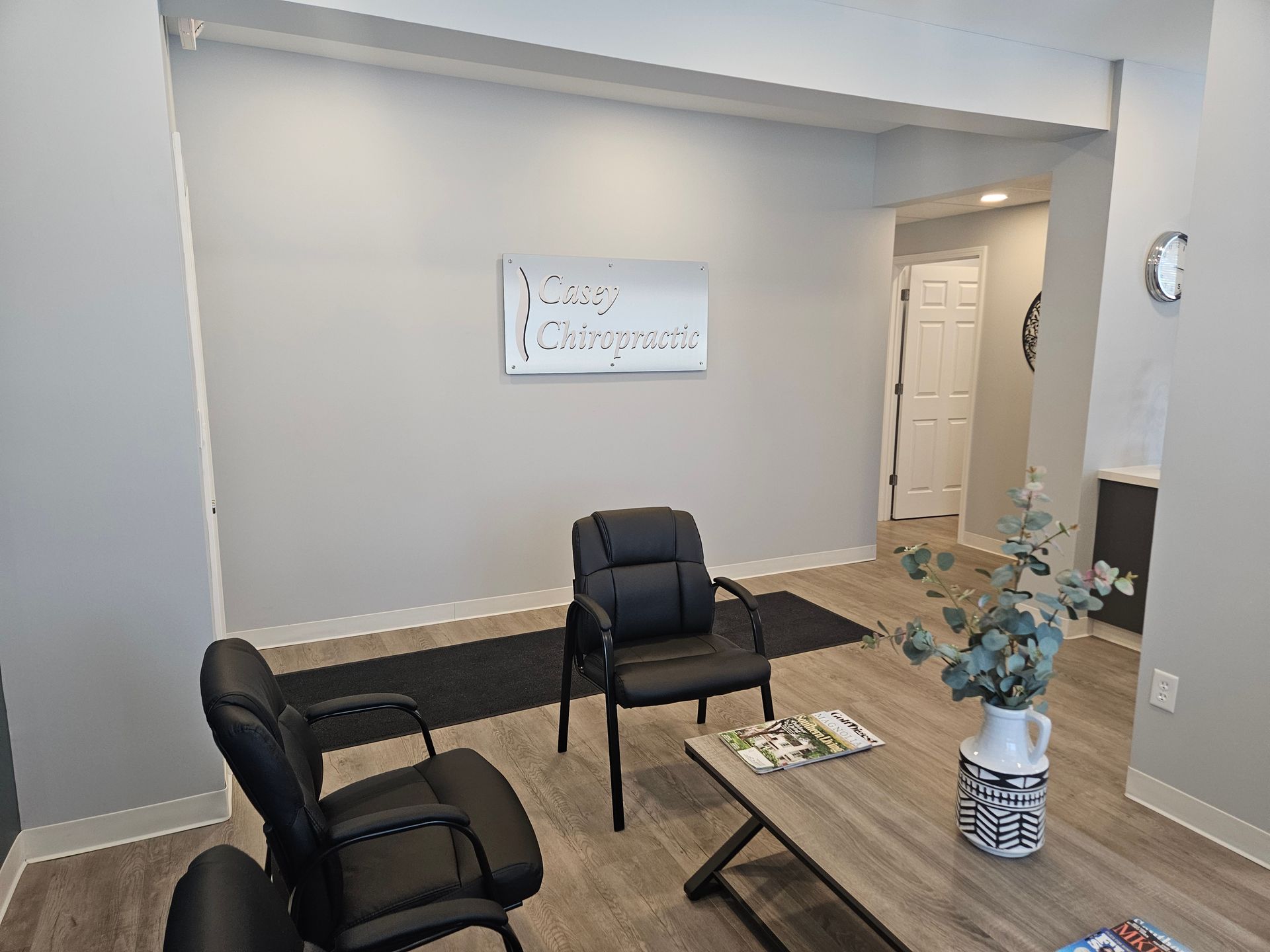 Small waiting room with two black chairs, a coffee table, wall art, and a hallway opening.