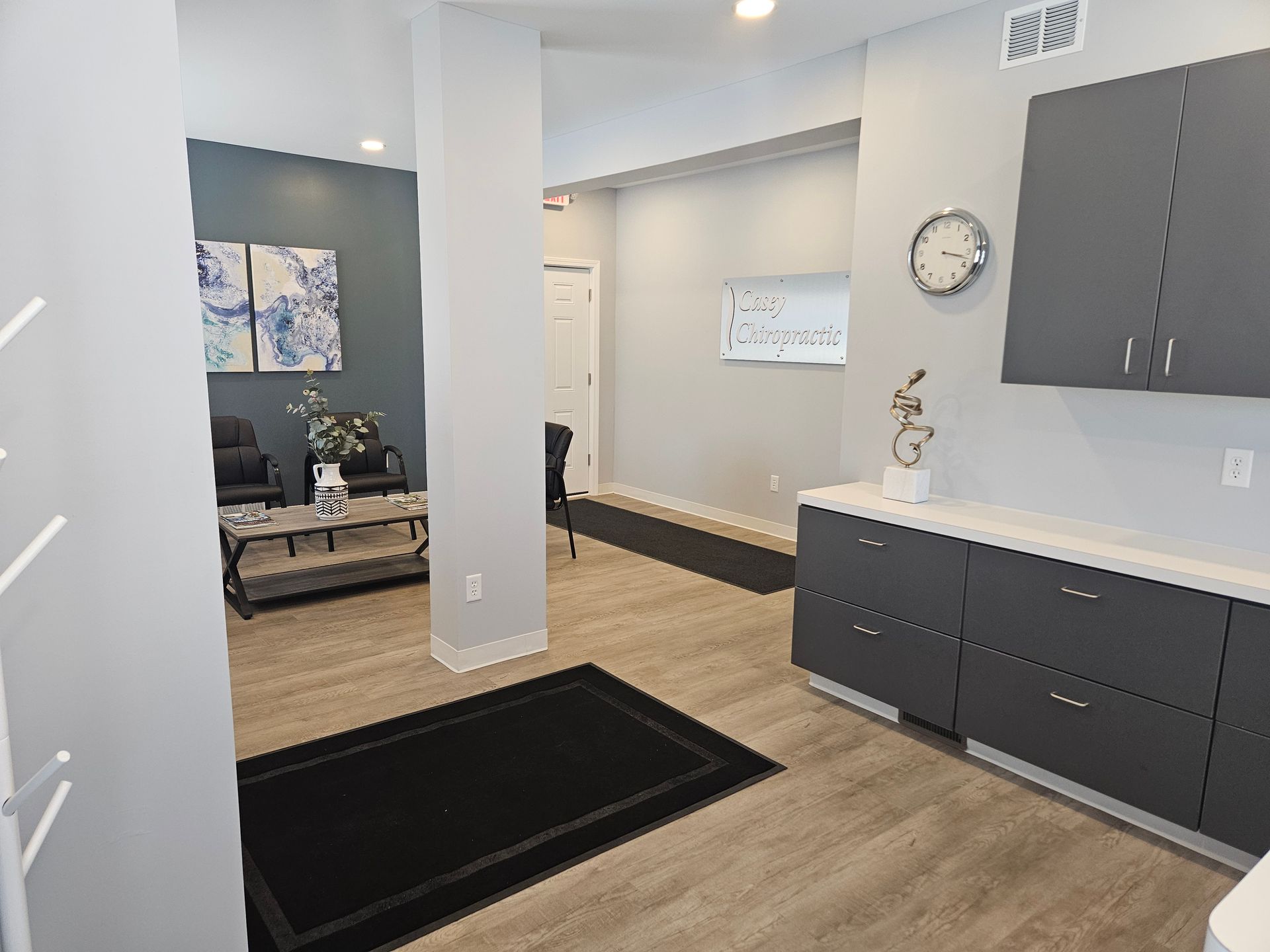 Modern office interior with gray cabinets, black rugs, and a seating area in the back.