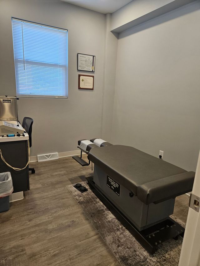 Small exam room with treatment table, window, and wall-mounted frames.