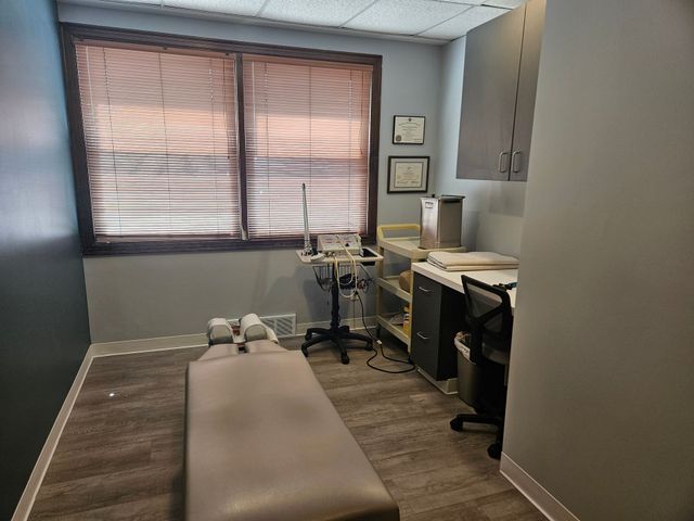 Exam room with treatment table, desk, medical equipment, and window with blinds