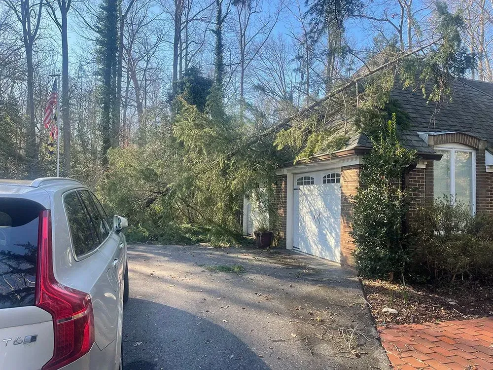Silver SUV in a driveway beside a brick garage and wooded yard on a sunny day
