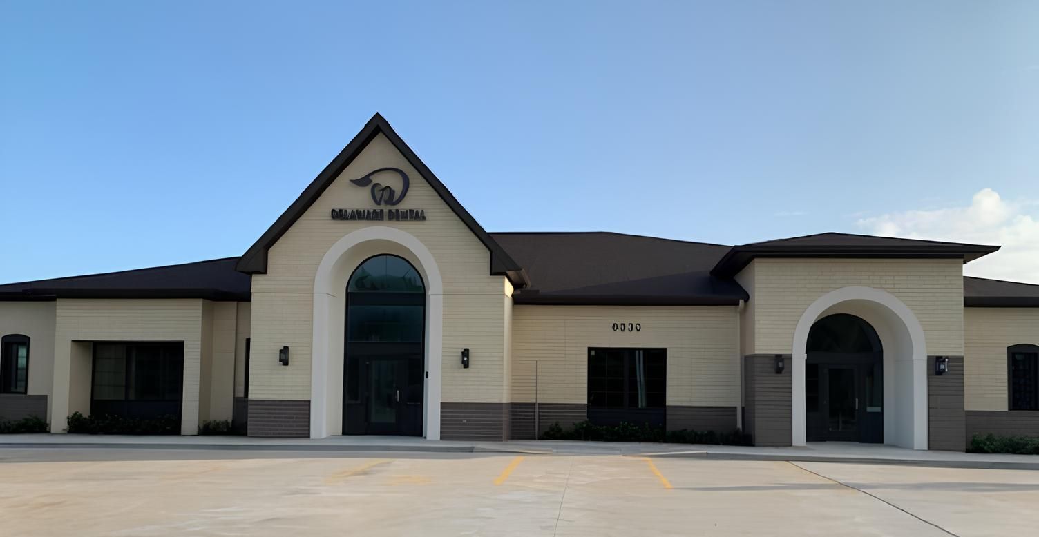 A large white building with a black roof is sitting on top of a concrete driveway.