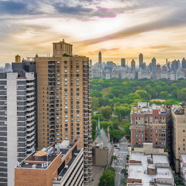 City skyline with tall apartment buildings and a green park under a warm sunset sky