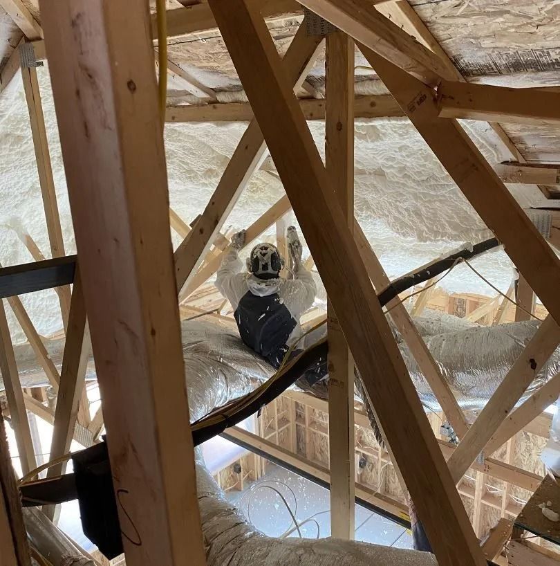 A person in protective gear spraying insulation in a wooden attic.