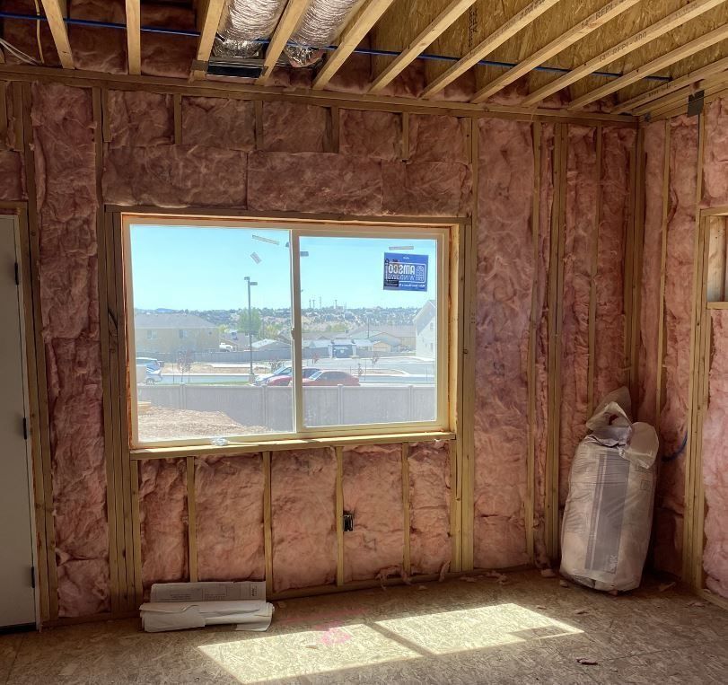 Interior of a building under construction; insulation in walls, window with a view, and a bag on the floor.
