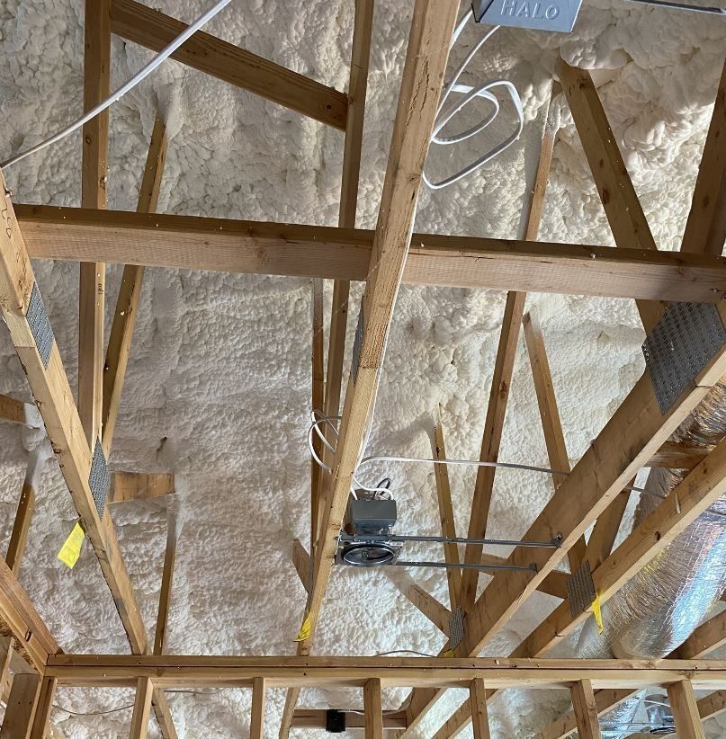 Wooden roof trusses with spray foam insulation, electrical wiring, and conduit in an attic.