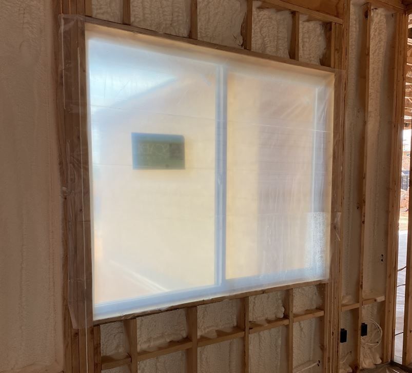 Window frame under construction, covered in plastic sheeting, interior view of a house.