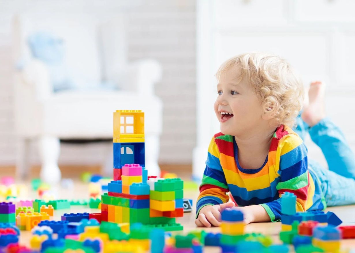 Child playing with colorful building blocks on the floor, smiling in a bright room