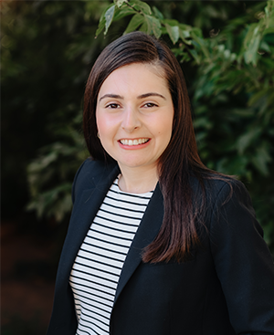 Maya Bismar wearing a striped shirt and a black jacket is smiling for the camera.
