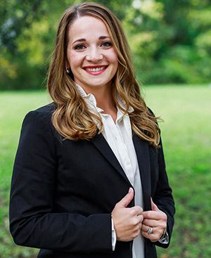 Megan Procter in a suit and white shirt is standing in a field.