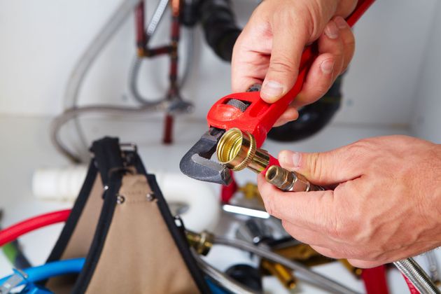 Hands using red wire cutters to strip a brass cable connector on a bicycle repair bench