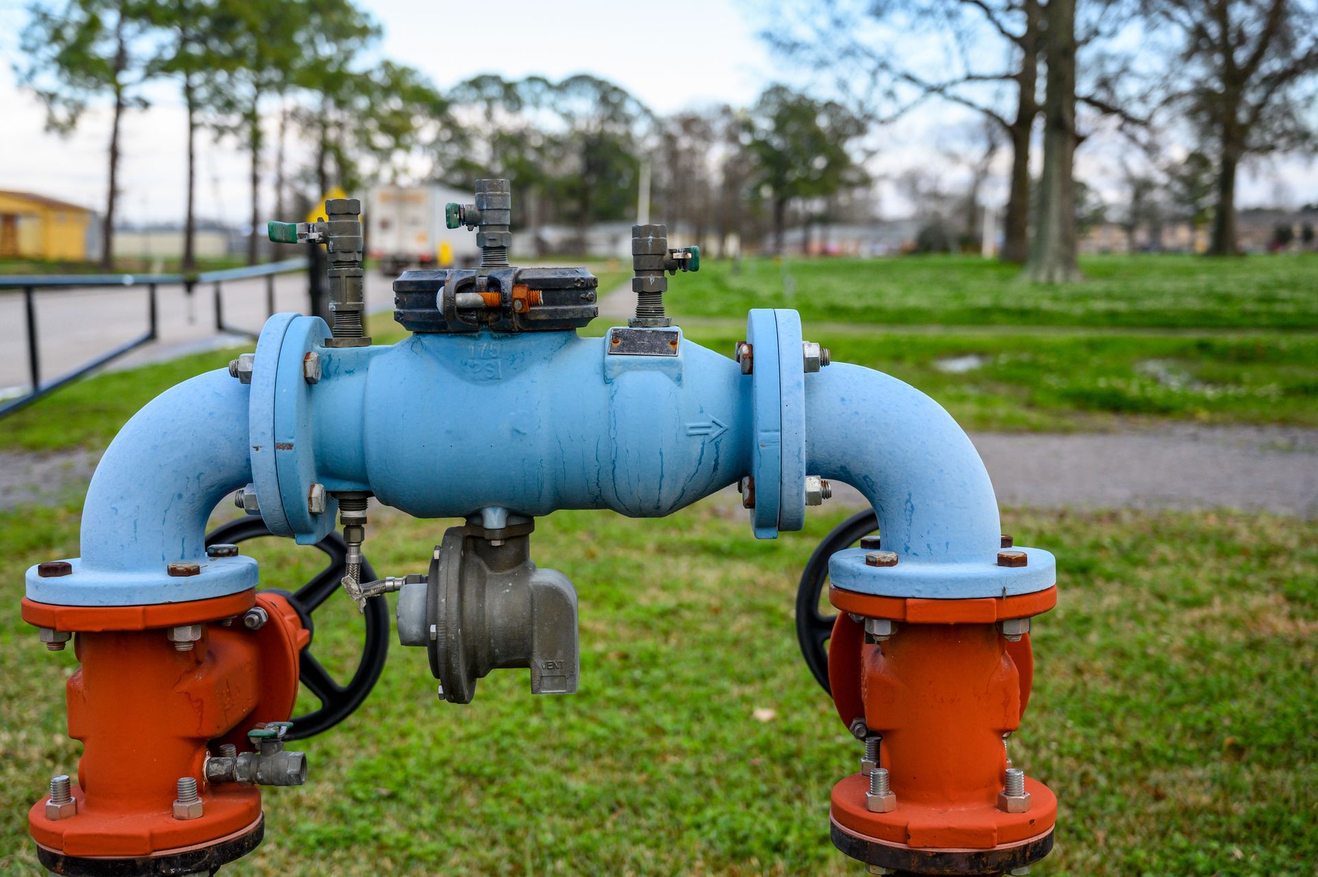 Blue pipeline with orange valves and silver gauge in a grassy outdoor utility area