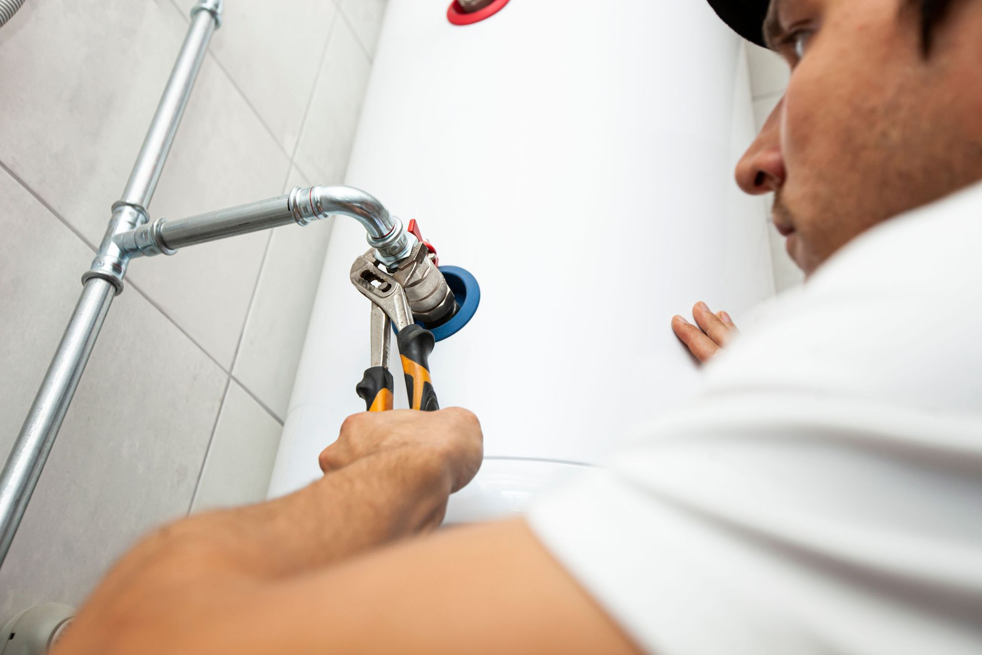 Plumber tightening a pipe valve with a wrench in a white bathroom or utility room