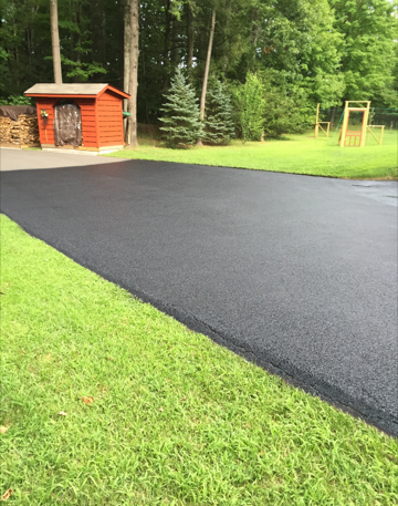A black driveway with a red shed in the background