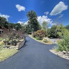 A driveway leading to a house surrounded by trees and bushes on a sunny day.