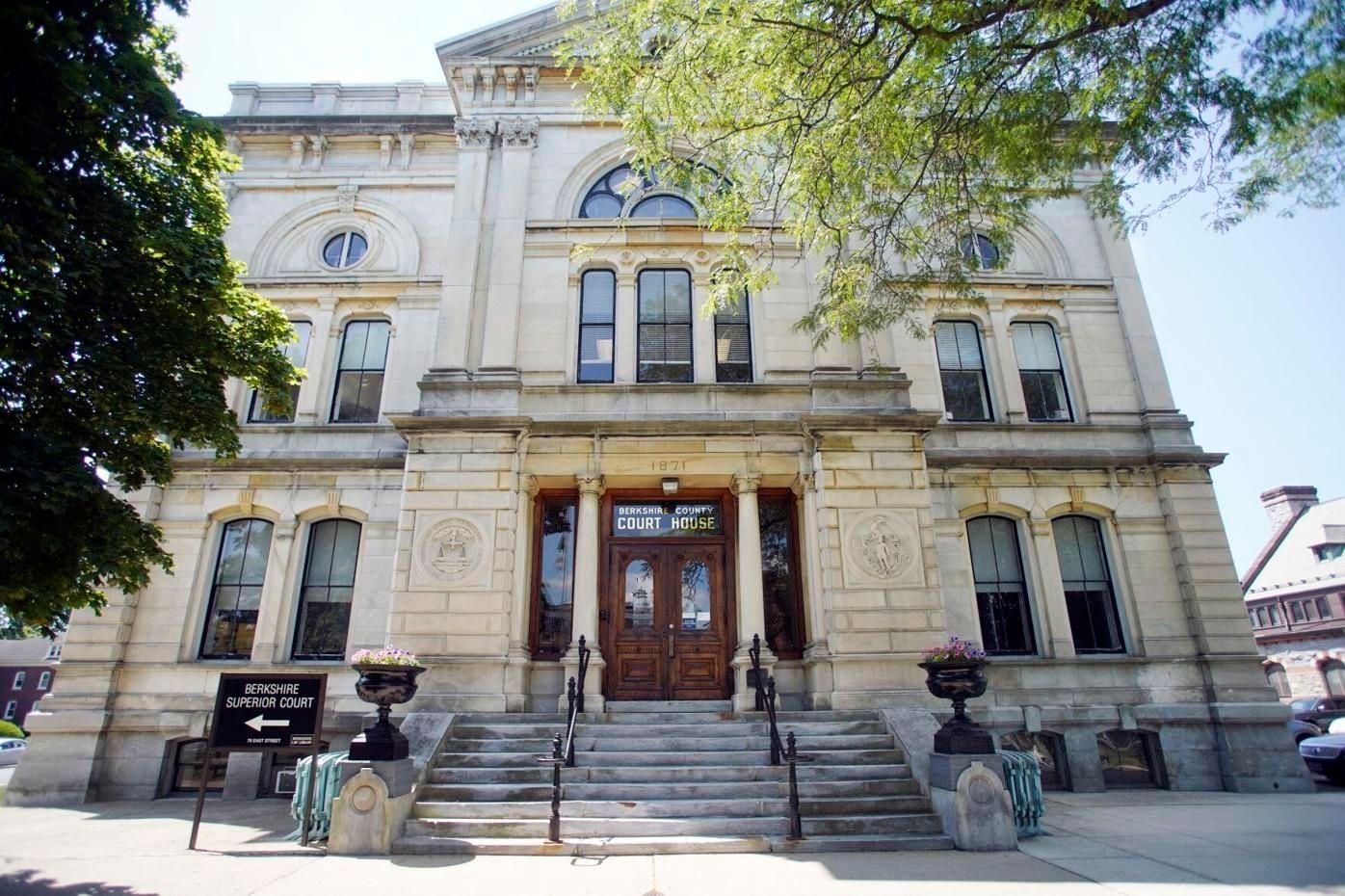 A cream-colored, multi-story historic stone building with a central staircase leading to a wooden double-door entrance.