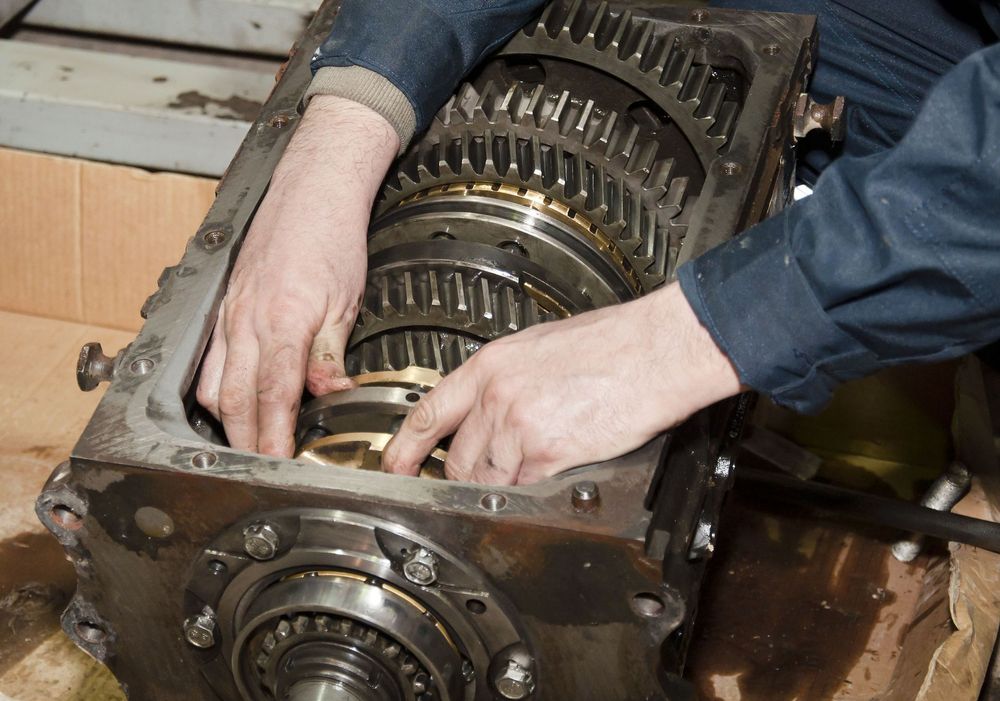 A mechanic’s hands work inside an open metal transmission casing, aligning internal gears and components.