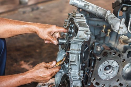 A person&rsquo;s hands clean the internal components of a disassembled engine block in an automotive repair shop.