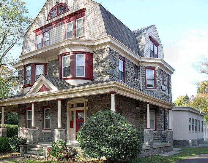 Stone multi-story house with red trim, porch, and a small outbuilding.