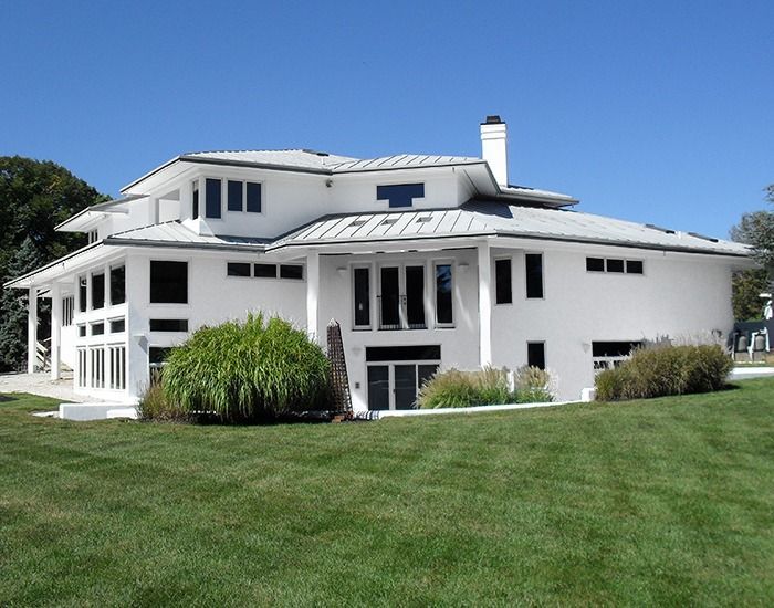 White modern house with multiple windows and a gray roof on a green lawn under a blue sky.