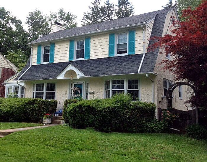 Two-story house with yellow siding, teal shutters, and a dark roof; front lawn with bushes.
