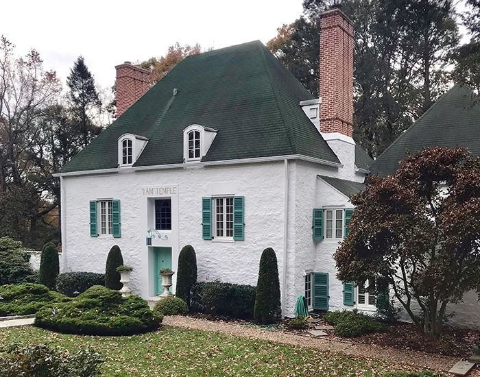 White two-story house with green roof and shutters, brick chimney, and manicured landscaping.