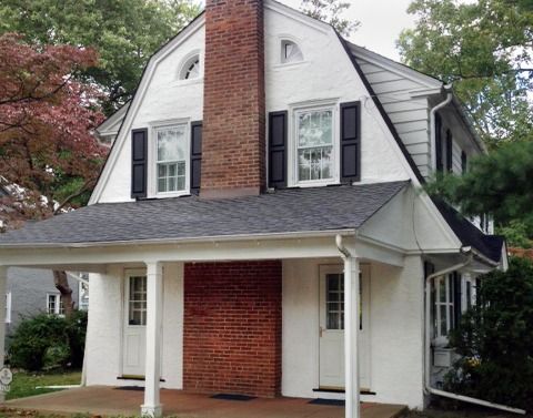 White house with a black roof and chimney. Brick accents and black shutters.
