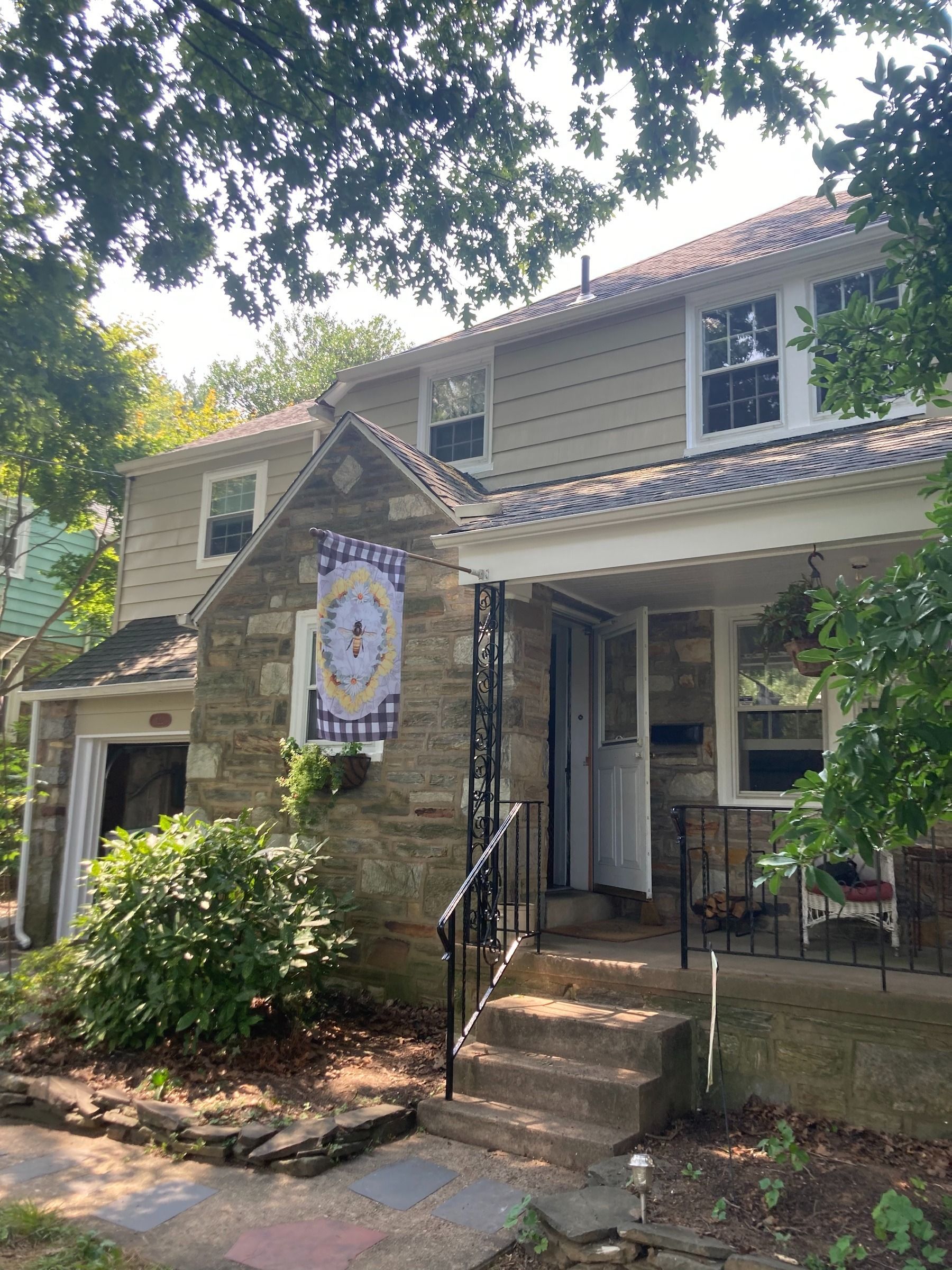 Two-story house with stone facade and beige siding. Steps lead to a covered porch with a hanging banner.