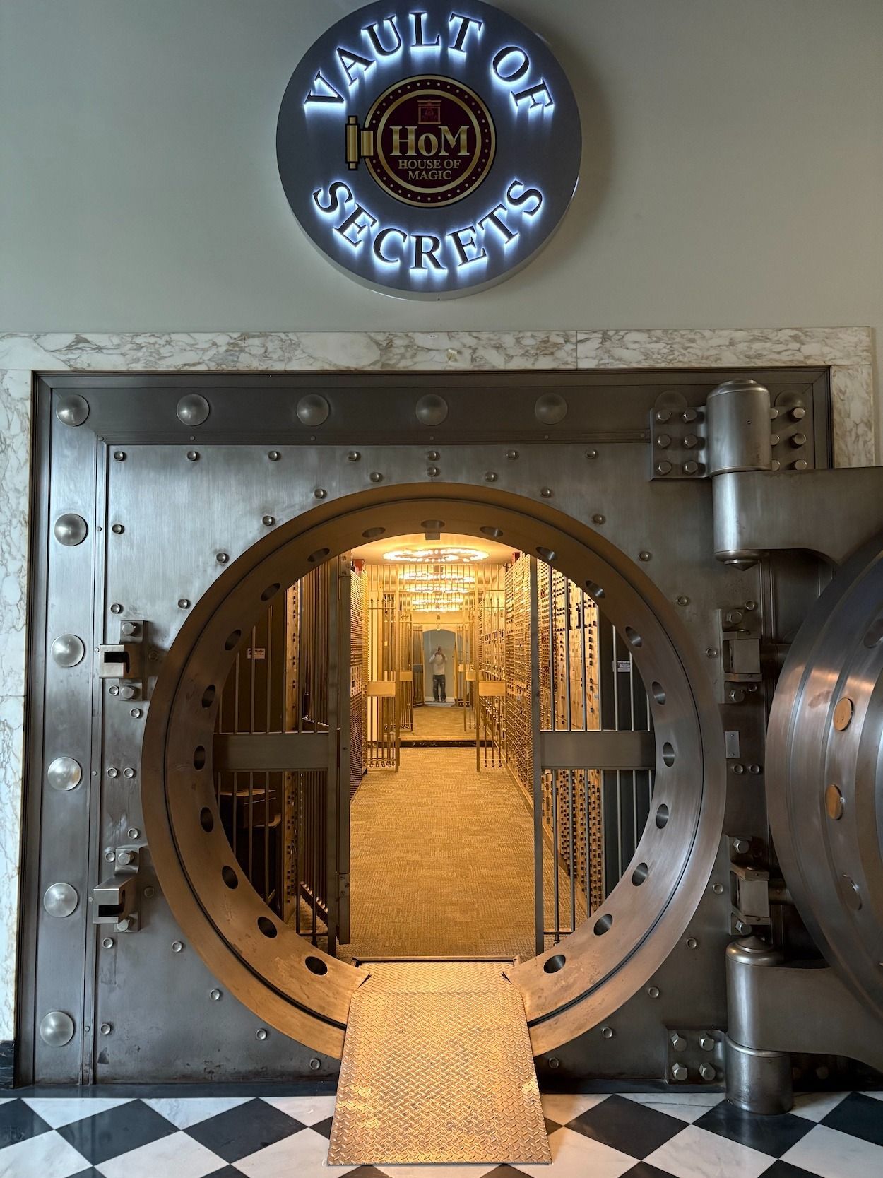 A large vault door with an open circular entrance leading to a long hallway. Sign above reads 