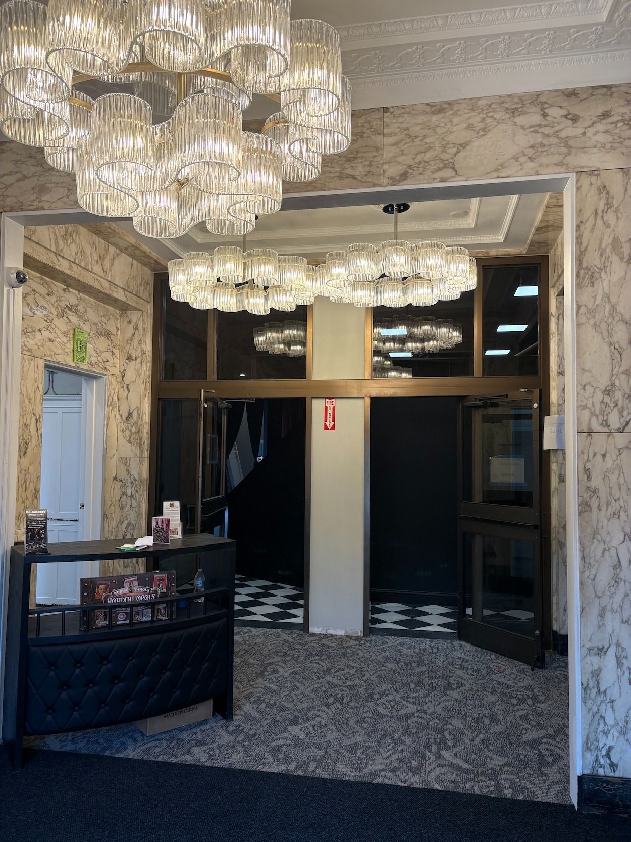 Grand lobby with large crystal chandeliers, checkered floor, marble walls, and a small service counter.