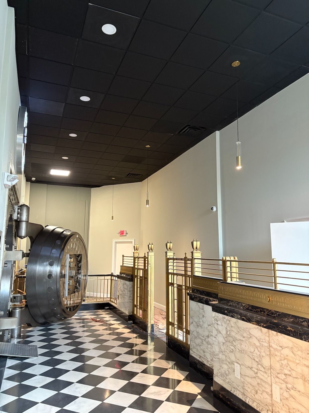 Interior of a former bank with a large vault door, black and white checkered floor, and golden accents.