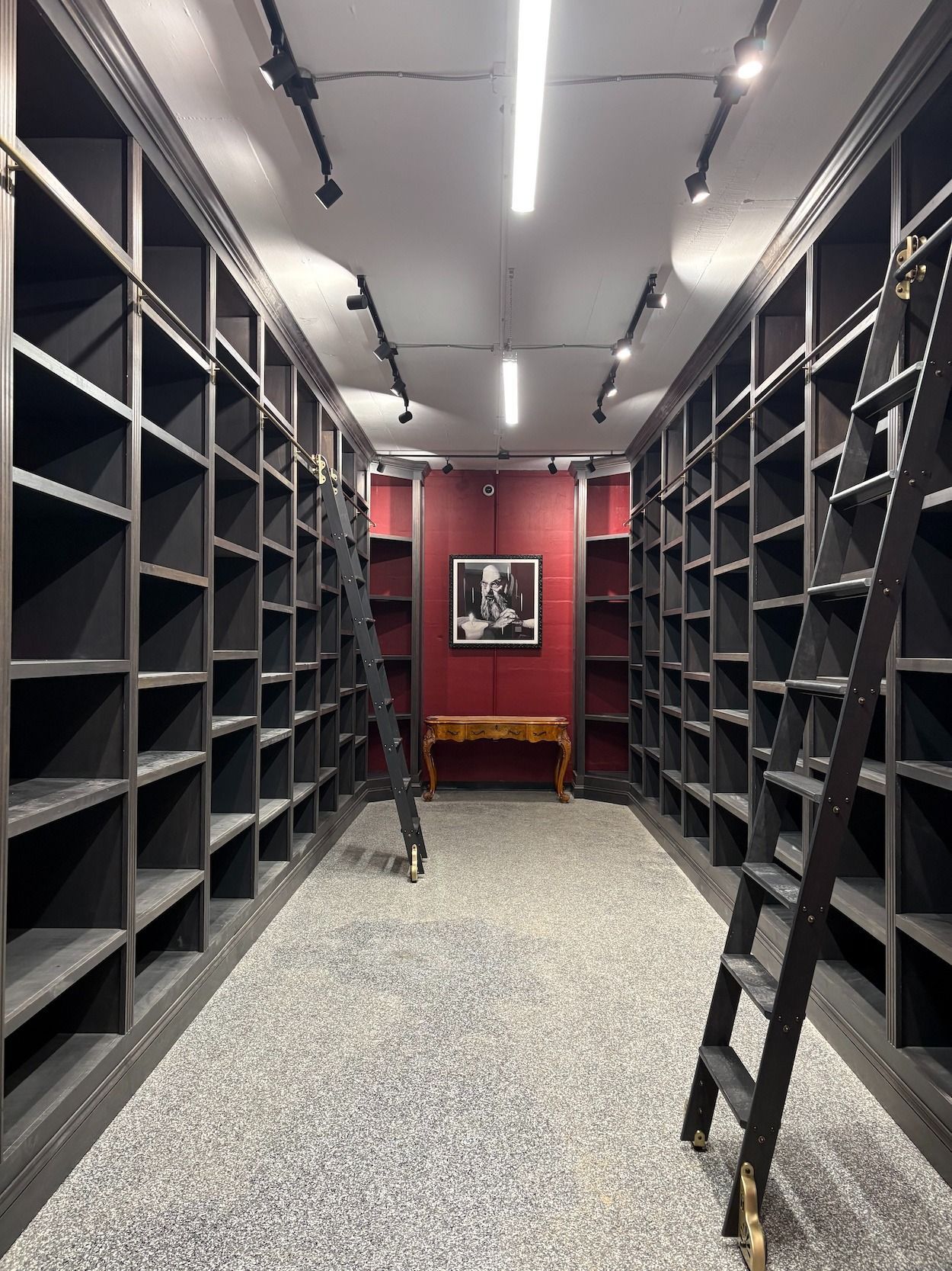 Library with dark shelves, red accent wall, two ladders, and a decorative table.