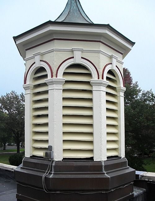 Octagonal white and beige cupola with horizontal slats for ventilation, atop a dark, multi-tiered base.