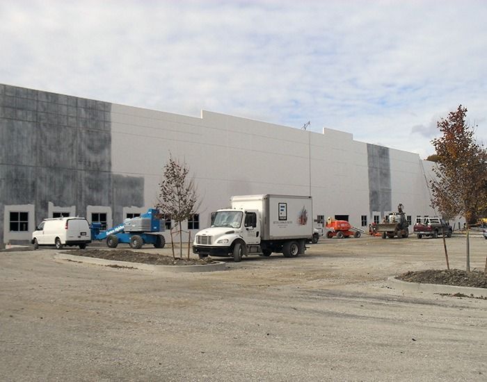 A large white warehouse under construction with several trucks and equipment parked in front.