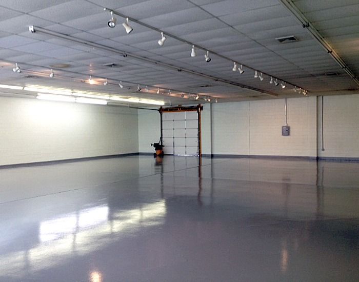 Empty industrial space with glossy gray floor and white walls. Garage door visible at the rear.
