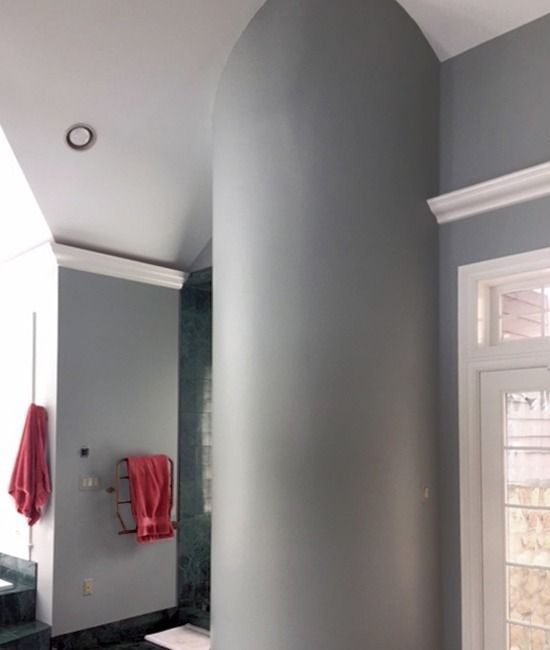 Bathroom with gray walls, white trim, arched ceiling. Red towels hang, natural light from window.